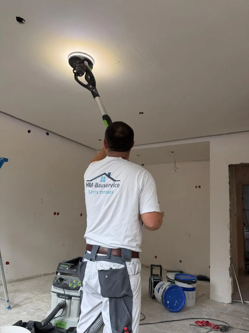 Handwerker schleift eine Zimmerdecke mit einem Deckenschleifer